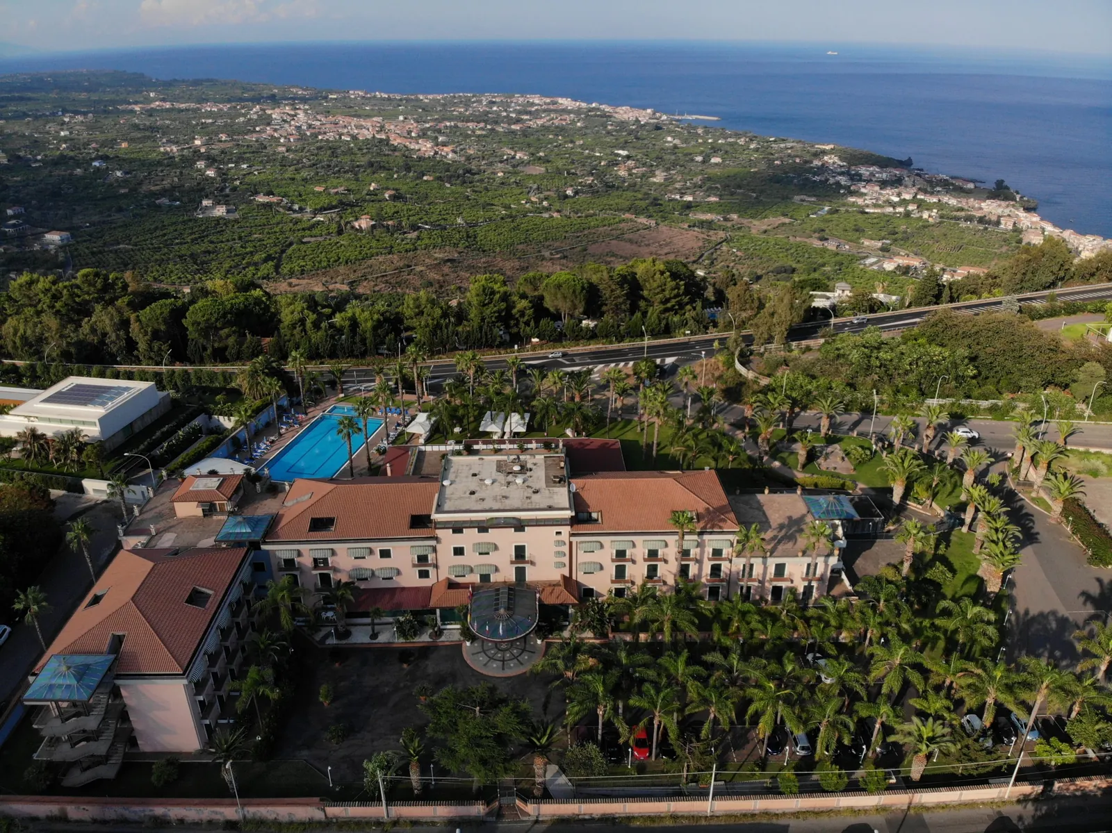 Vista aerea dell'Hotel Orizzonte: il parco con le palme, le piscine e, sopra la linea, la costa e il mare di Acireale