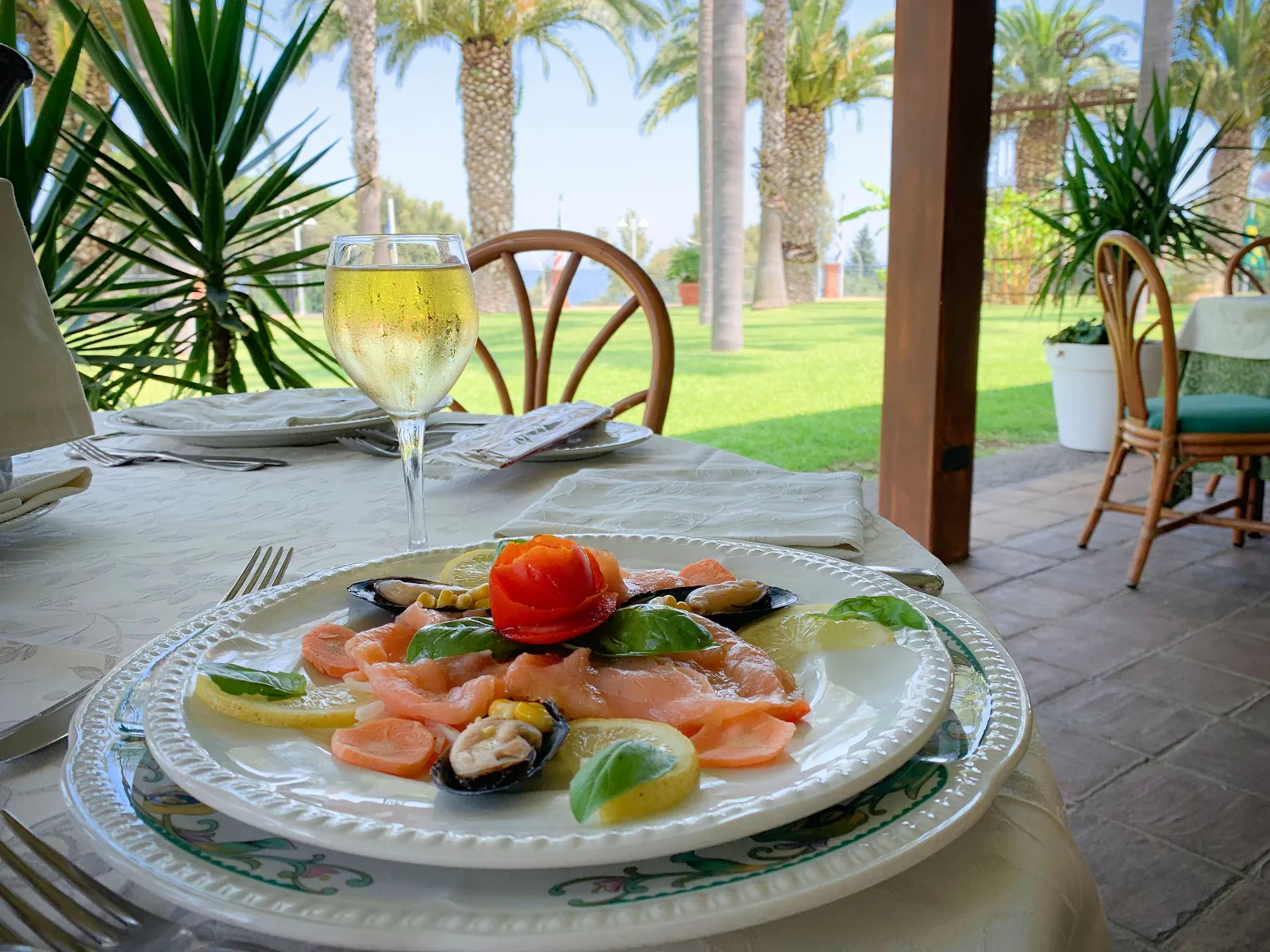 La tavola apparecchiata della terrazza, con il piatto di salmone e, dietro le palme, la linea del mare